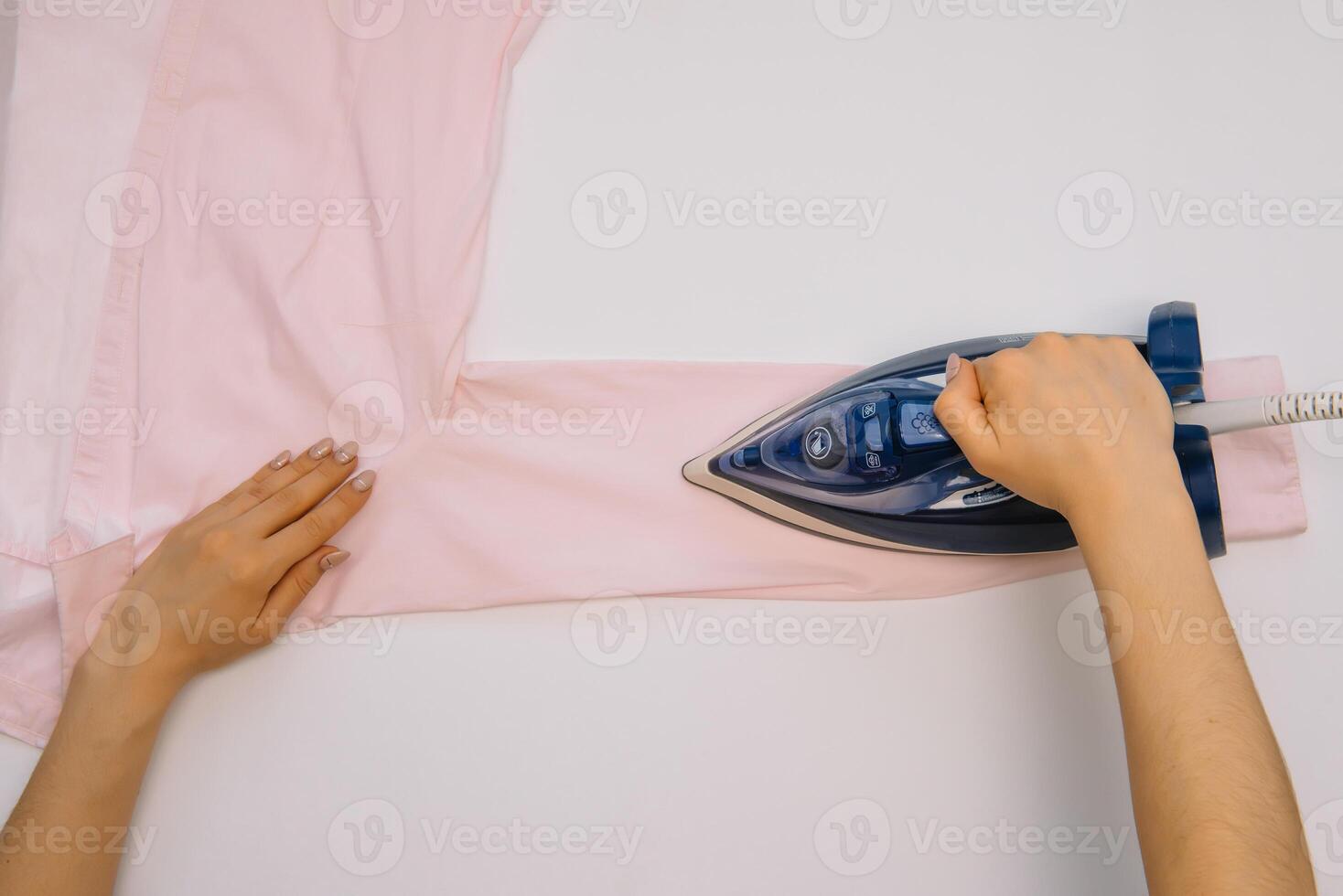 femelle main repassage vêtements Haut vue isolé sur blanc Contexte. Jeune femme avec le fer repassage homme chemise vu de au dessus pendant travaux ménagers. bleu le fer sur blanc table photo