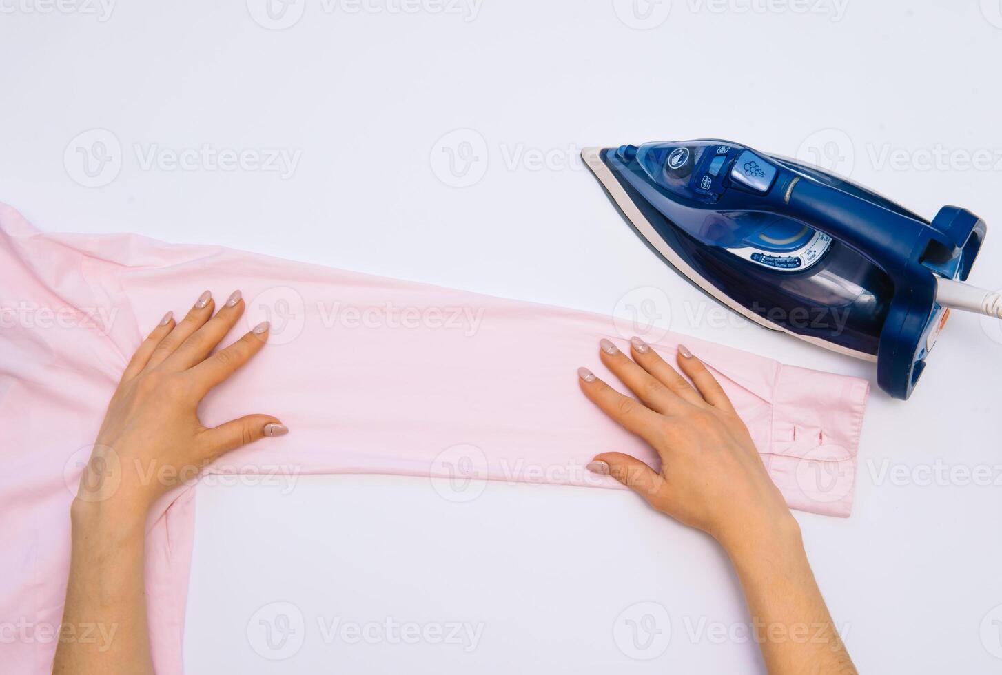 femelle main repassage vêtements Haut vue isolé sur blanc Contexte. Jeune femme avec le fer repassage homme chemise vu de au dessus pendant travaux ménagers. bleu le fer sur blanc table photo