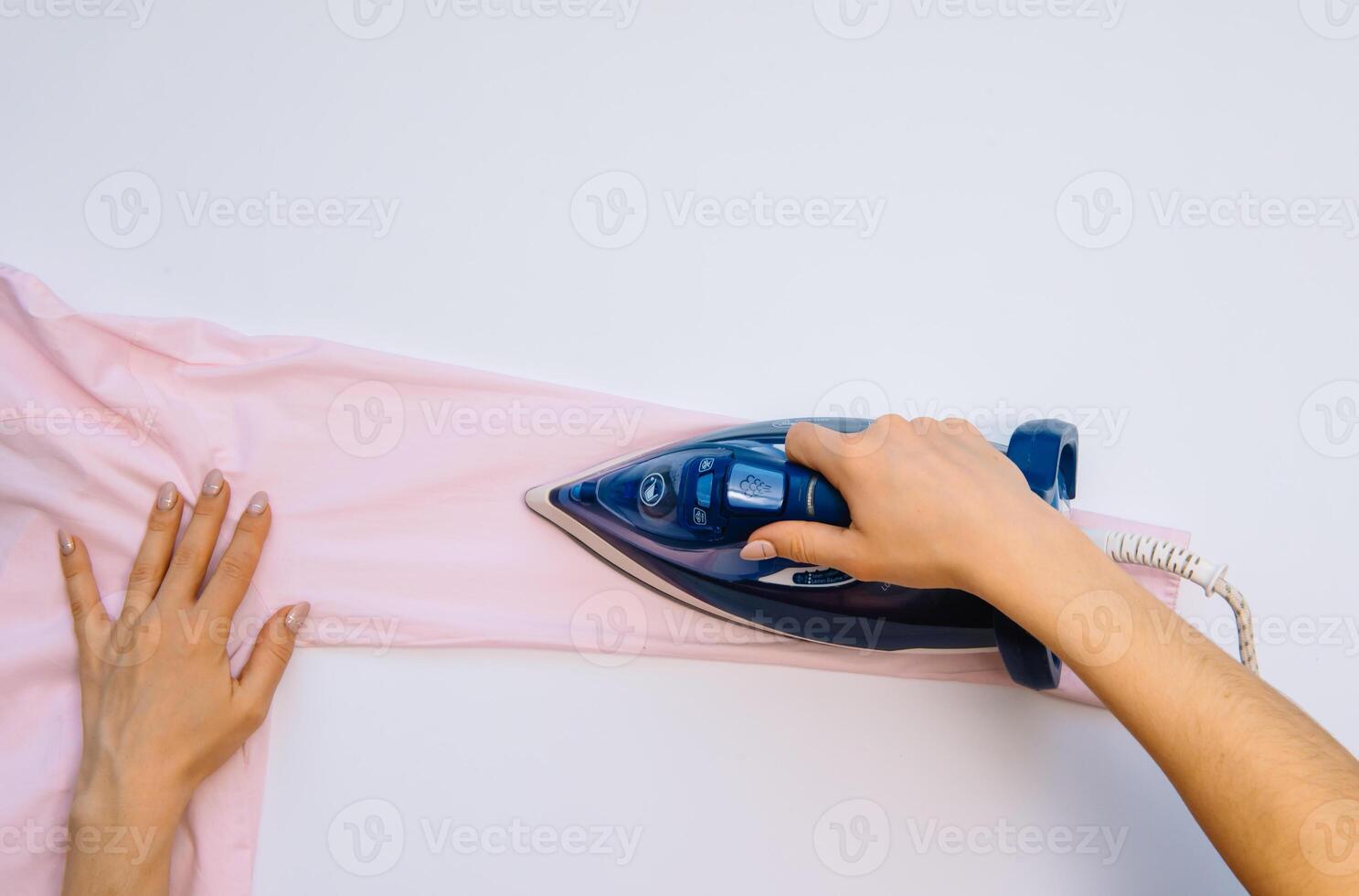 femelle main repassage vêtements Haut vue isolé sur blanc Contexte. Jeune femme avec le fer repassage homme chemise vu de au dessus pendant travaux ménagers. bleu le fer sur blanc table photo