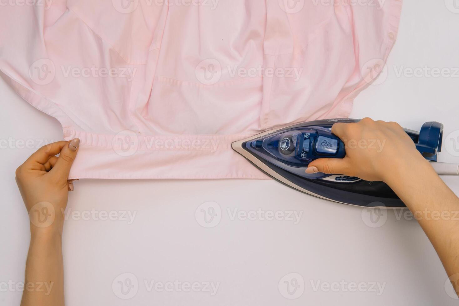 femelle main repassage vêtements Haut vue isolé sur blanc Contexte. Jeune femme avec le fer repassage homme chemise vu de au dessus pendant travaux ménagers. bleu le fer sur blanc table photo