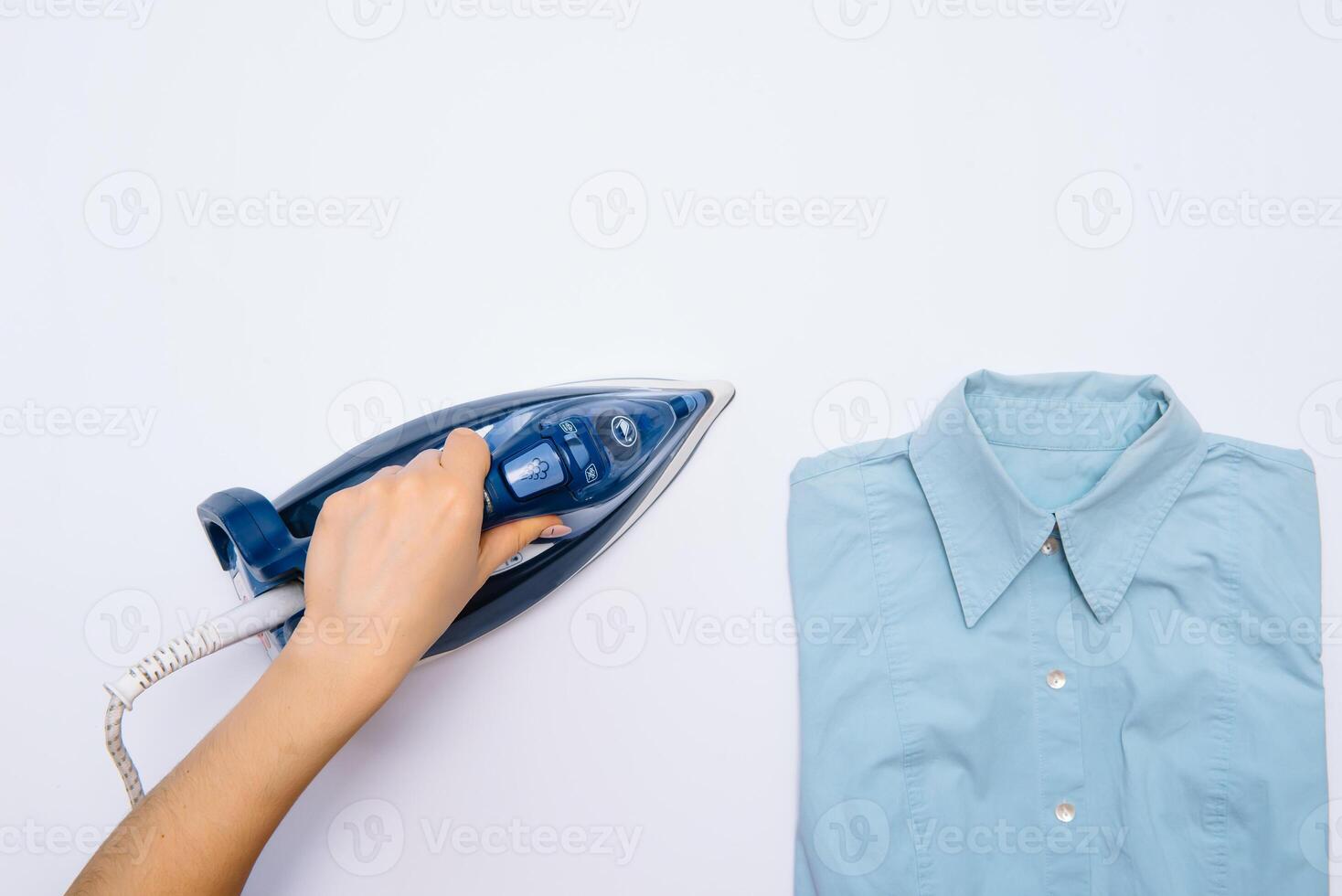 femelle main repassage vêtements Haut vue isolé sur blanc Contexte. Jeune femme avec le fer repassage homme chemise vu de au dessus pendant travaux ménagers. bleu le fer sur blanc table photo