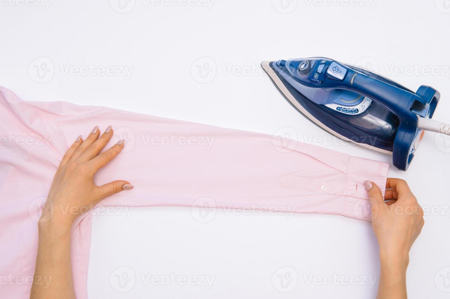 femelle main repassage vêtements Haut vue isolé sur blanc Contexte. Jeune femme avec le fer repassage homme chemise vu de au dessus pendant travaux ménagers. bleu le fer sur blanc table photo