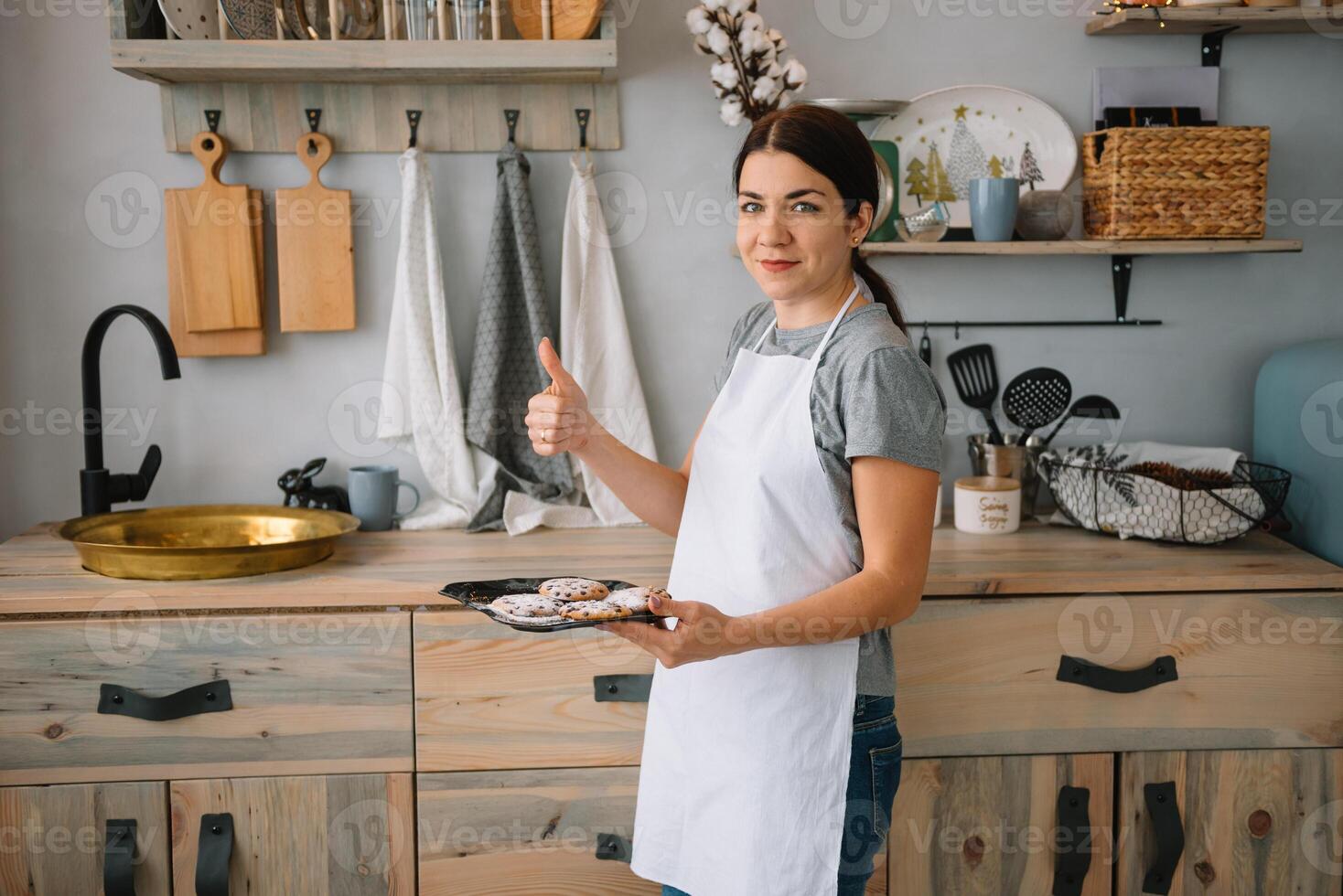 Jeune content maman et sa bébé cuisinier biscuits à Accueil dans le cuisine. Noël fait maison pain d'épice. mignonne garçon avec mère dans blanc uniforme et chapeau cuit Chocolat biscuits photo