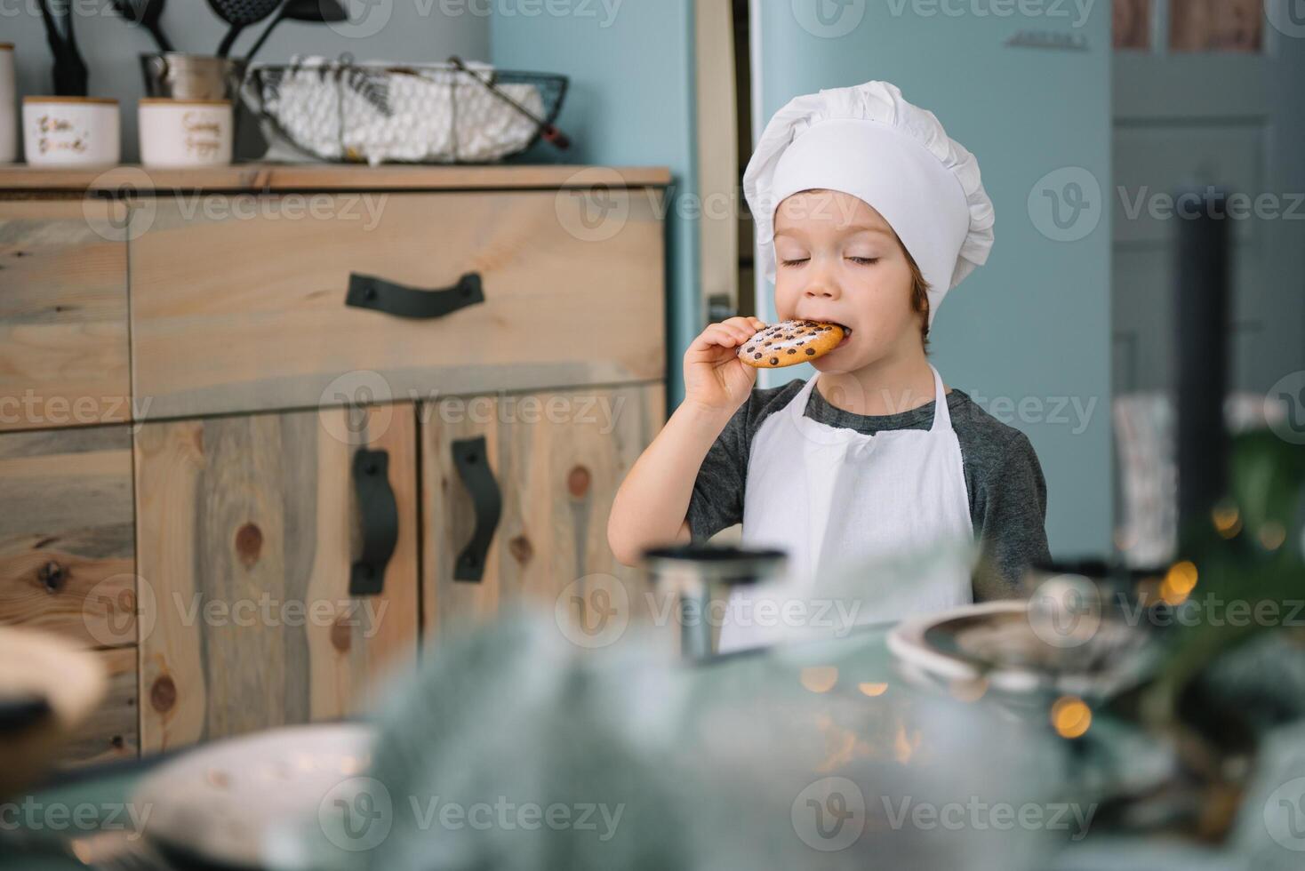 Jeune content maman et sa bébé cuisinier biscuits à Accueil dans le cuisine. Noël fait maison pain d'épice. mignonne garçon avec mère dans blanc uniforme et chapeau cuit Chocolat biscuits. photo