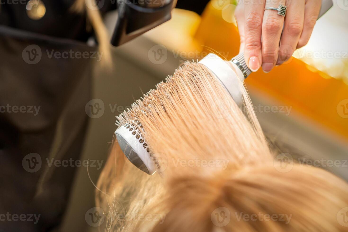 coiffeur main séchage blond cheveux avec une sèche-cheveux et rond brosse dans une beauté salon. photo