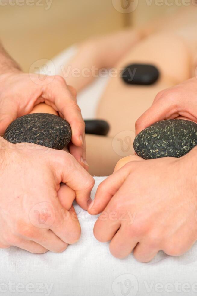 deux masseurs faire une pied massage avec une chaud pierre dans quatre mains à le spa. photo