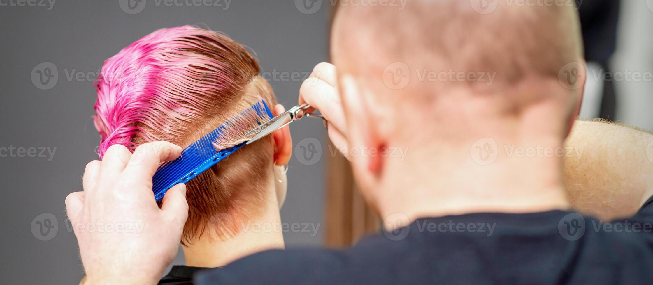 femme ayant une Nouveau la Coupe de cheveux. Masculin coiffeur Coupe rose court cheveux avec les ciseaux dans une cheveux salon. photo