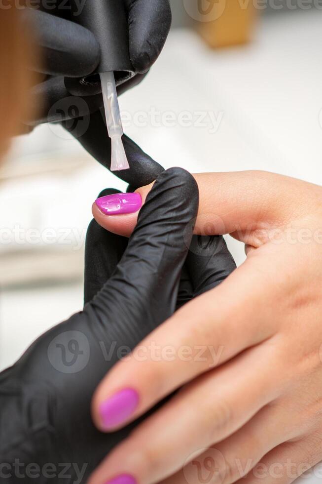 La peinture ongles de une femme. mains de manucure dans noir gants appliquant rose clou polonais sur femelle ongles dans une beauté salon. photo