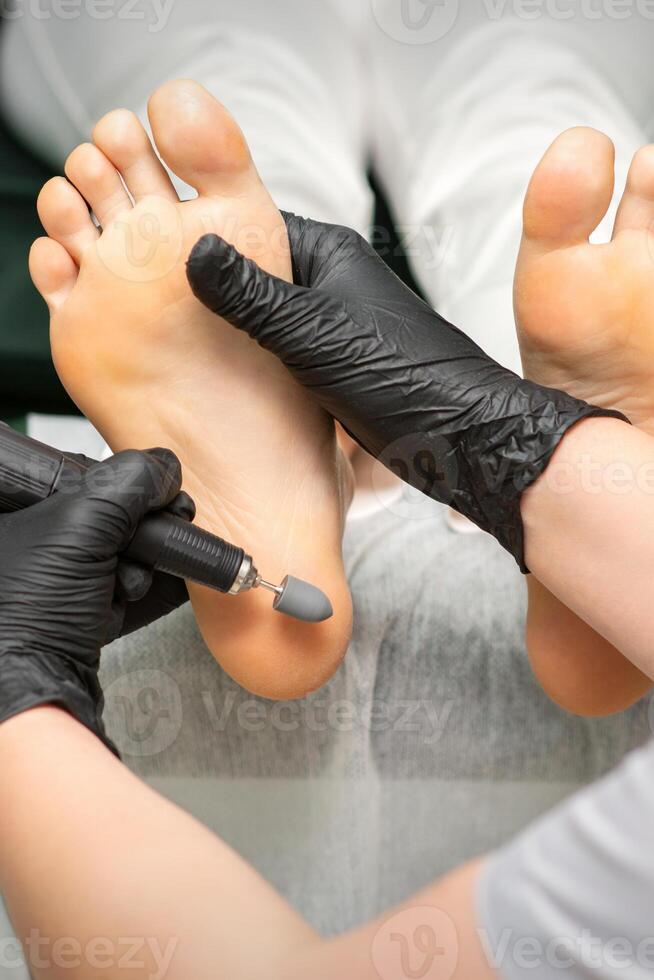peeling femelle pieds. mains de podologie spécialiste dans noir gants en utilisant spécial broyage équipement polonais femelle pied de cal et blé dans le beauté salon. photo