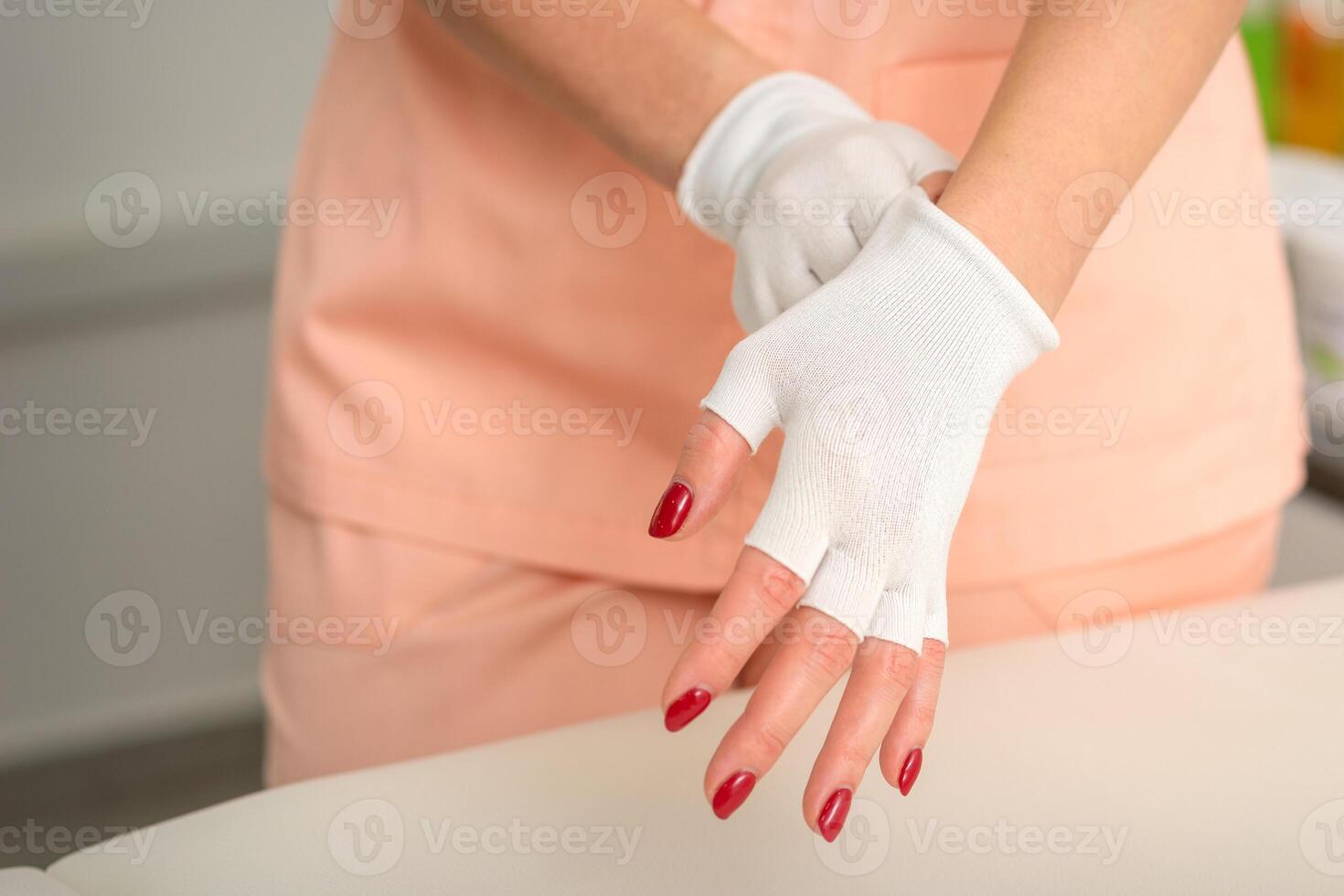 esthéticienne dans vêtements de travail portant blanc bambou sans doigts gants sur sa mains dans une beauté salon. photo