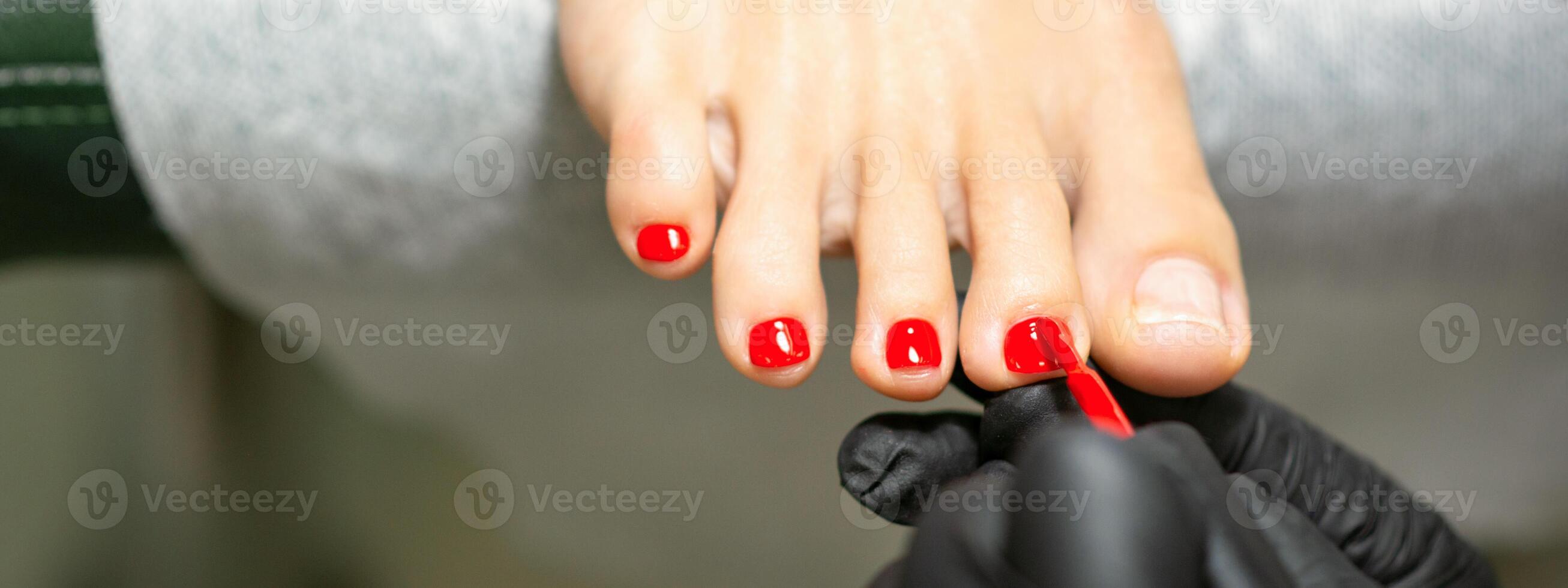 pédicure appliquant rouge clou polonais à le femelle les ongles dans une beauté salon. photo