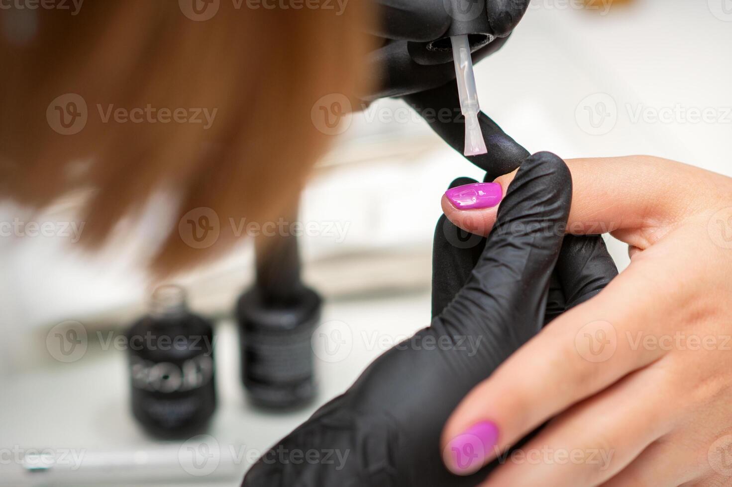 La peinture ongles de une femme. mains de manucure dans noir gants appliquant rose clou polonais sur femelle ongles dans une beauté salon. photo