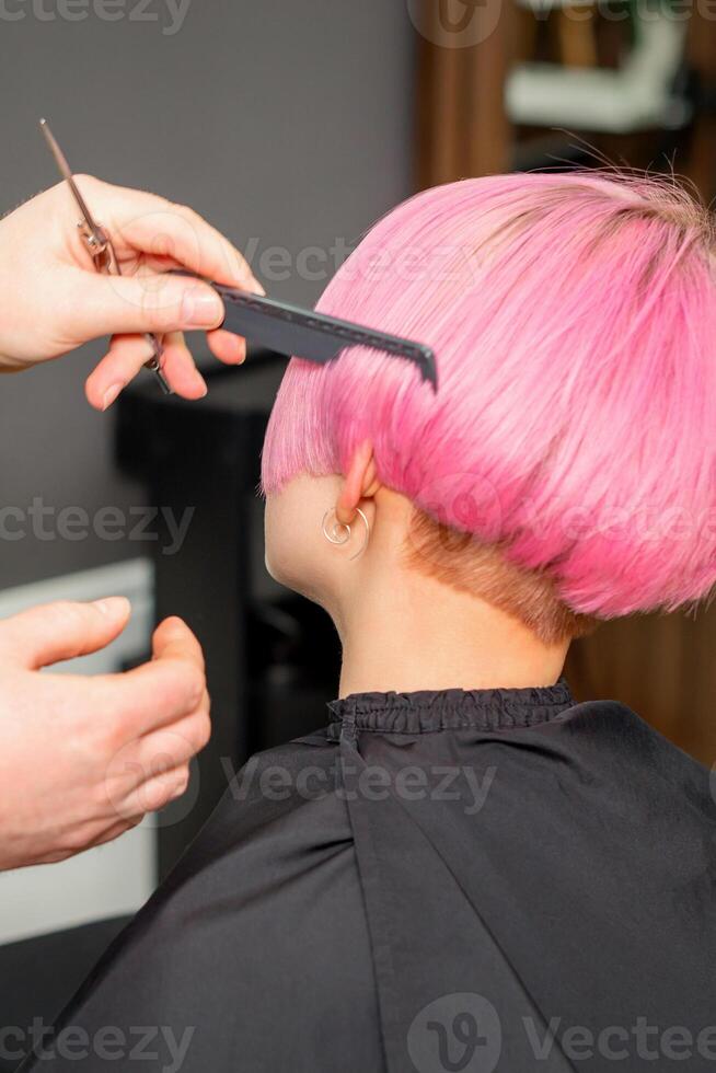 mains de coiffeur ratissage cheveux fabrication court rose coiffure pour une Jeune caucasien femme dans une beauté salon. photo