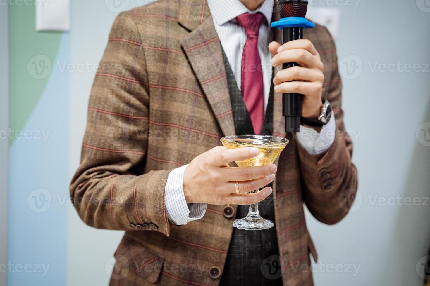 une main détient une verre de Champagne, une martini est versé dans une verre, une homme dit une pain grillé dans une microphone, une affaires homme dans une veste, une faire la fête, un un événement présentation. photo