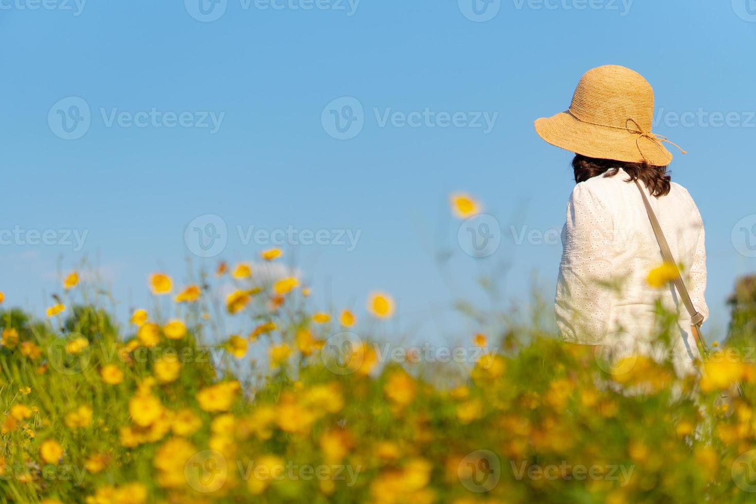 Femme portant un chapeau de paille marchant dans un champ de fleurs jaunes sous un ciel bleu en été photo