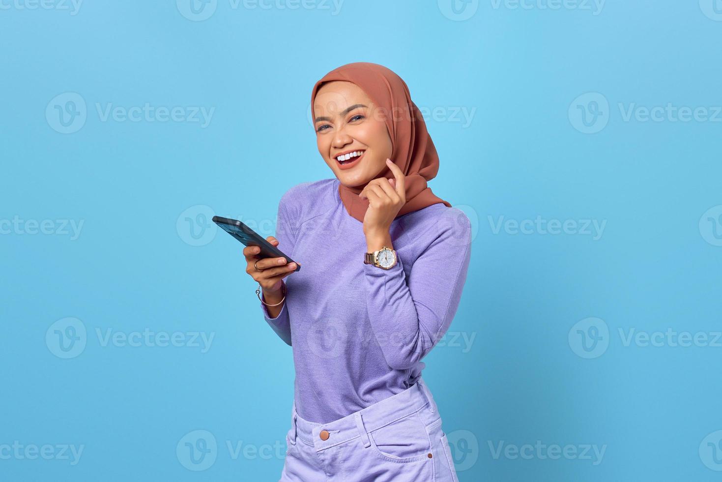 Portrait de jeune femme asiatique souriante à l'aide d'un téléphone portable sur fond bleu photo