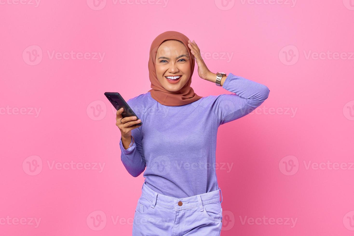 Portrait de jeune femme asiatique souriante tenant un téléphone portable sur fond rose photo