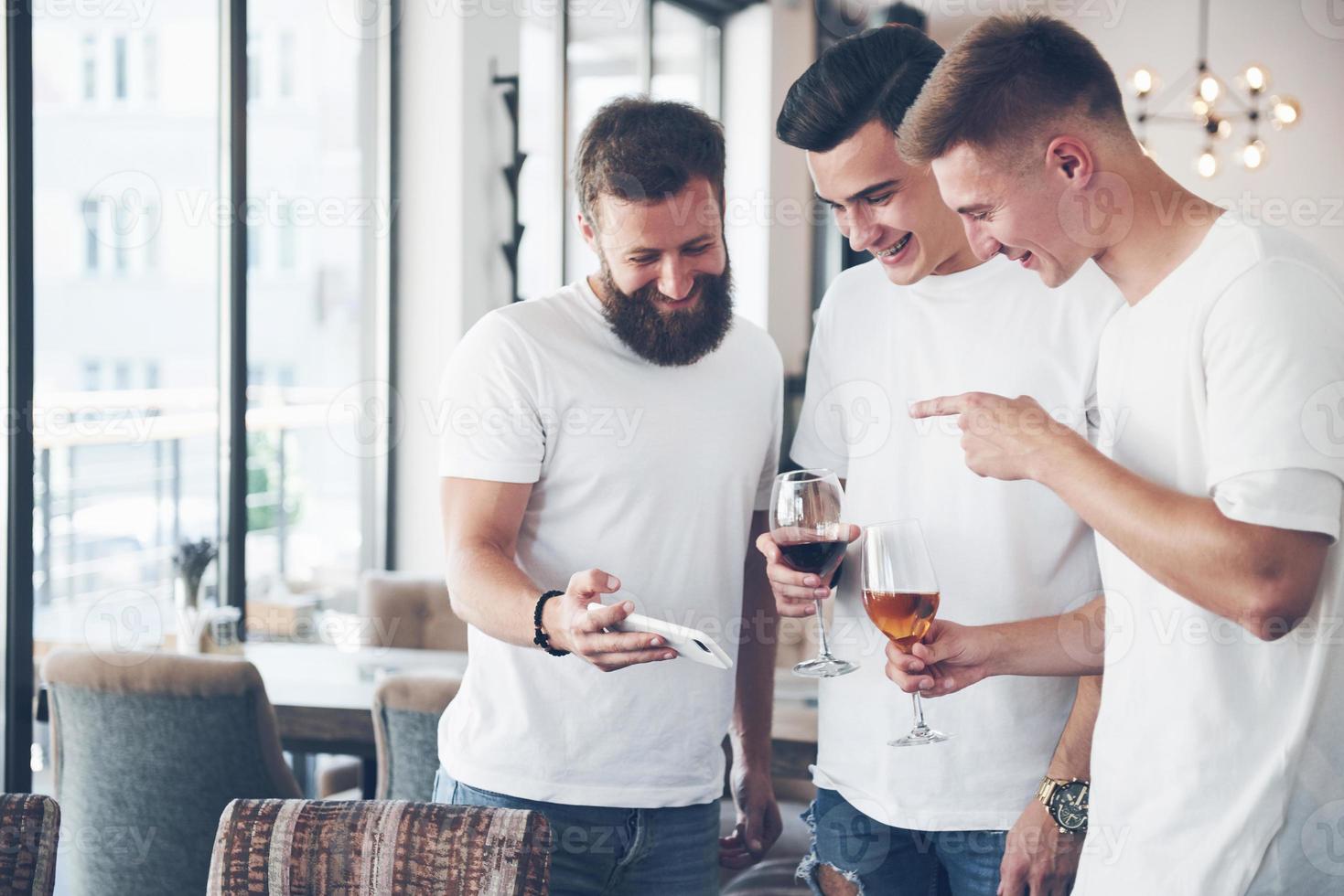 de vieux amis joyeux communiquent entre eux et regardent le téléphone, avec des verres de whisky ou de vin au pub. concept de divertissement et de style de vie. personnes connectées wifi en réunion de table de bar photo