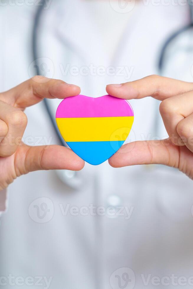 pansexuel fierté journée et lgbt fierté mois concept. médecin main en portant rose, Jaune et bleu cœur forme pour lesbienne, gay, bisexuel, transgenres, queer et pansexuel communauté photo