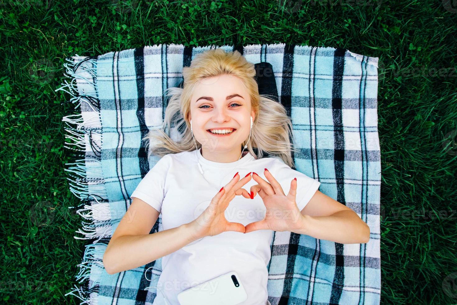 femme dans les écouteurs et smartphone faisant des mains symbole de coeur allongé sur fond vert photo