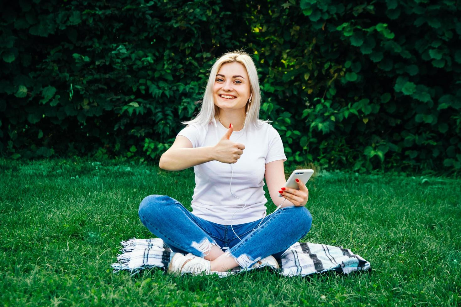 femme dans les écouteurs et smartphone dans les mains sur l'herbe verte photo