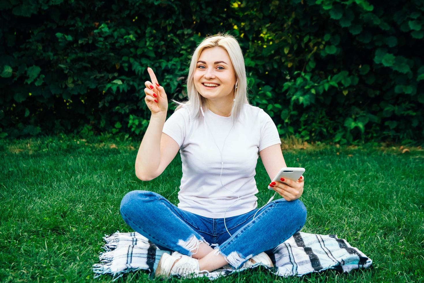 femme dans les écouteurs et smartphone dans les mains sur l'herbe verte photo