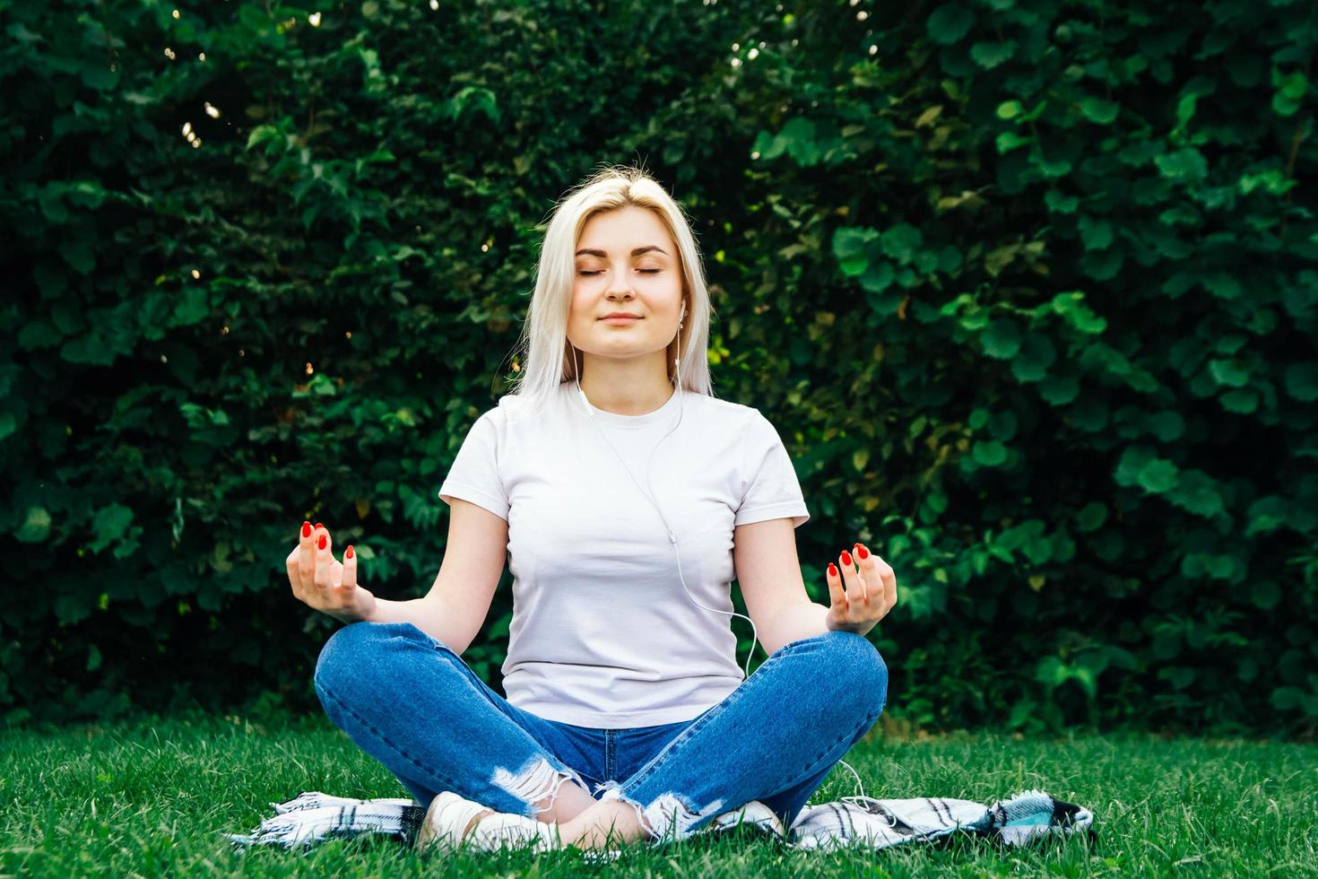 femme dans les écouteurs est assise dans une pose méditative sur l'herbe verte photo