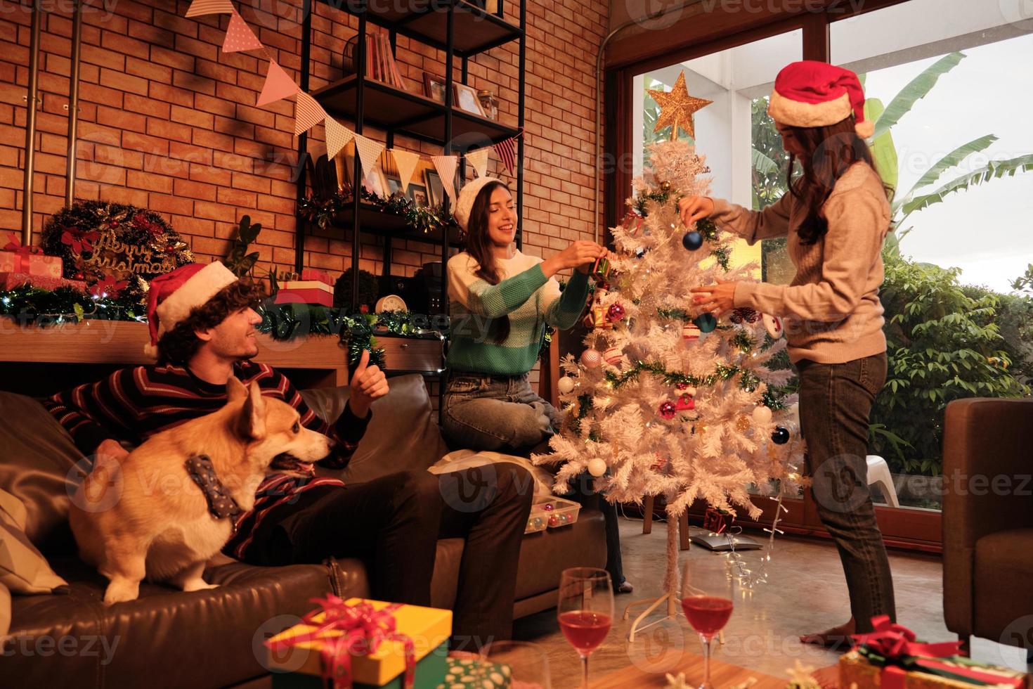 la famille avec un chien et des amis décorent joyeusement le sapin de Noël blanc dans le salon de la maison, se préparent de manière amusante et joyeuse pour une fête de célébration pour les vacances du festival du nouvel an. photo