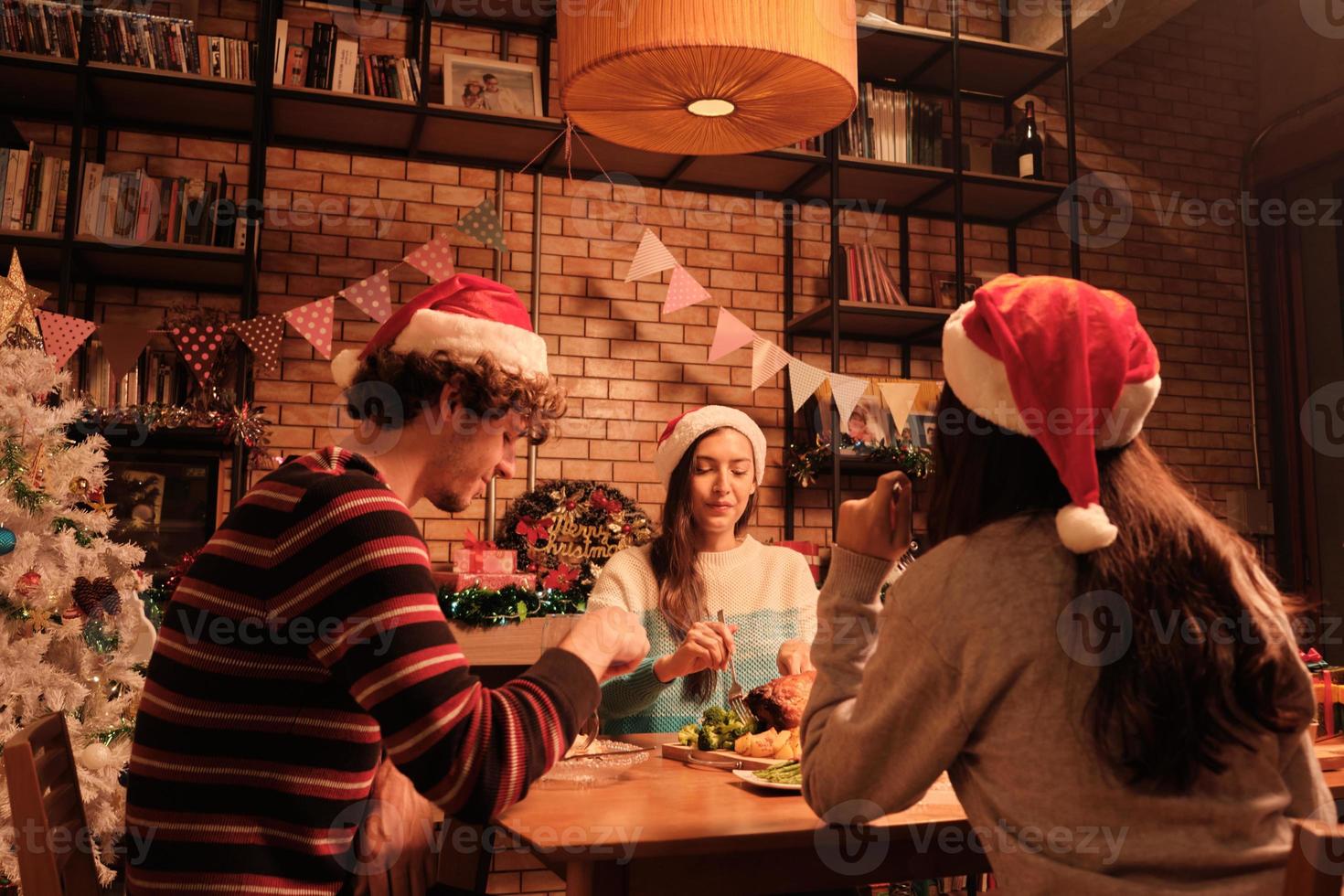 les amis s'amusent à dîner à table avec des aliments spéciaux, tels que la dinde rôtie et le vin dans la salle à manger de la maison, décorée d'ornements, le festival de Noël et la fête du nouvel an. photo