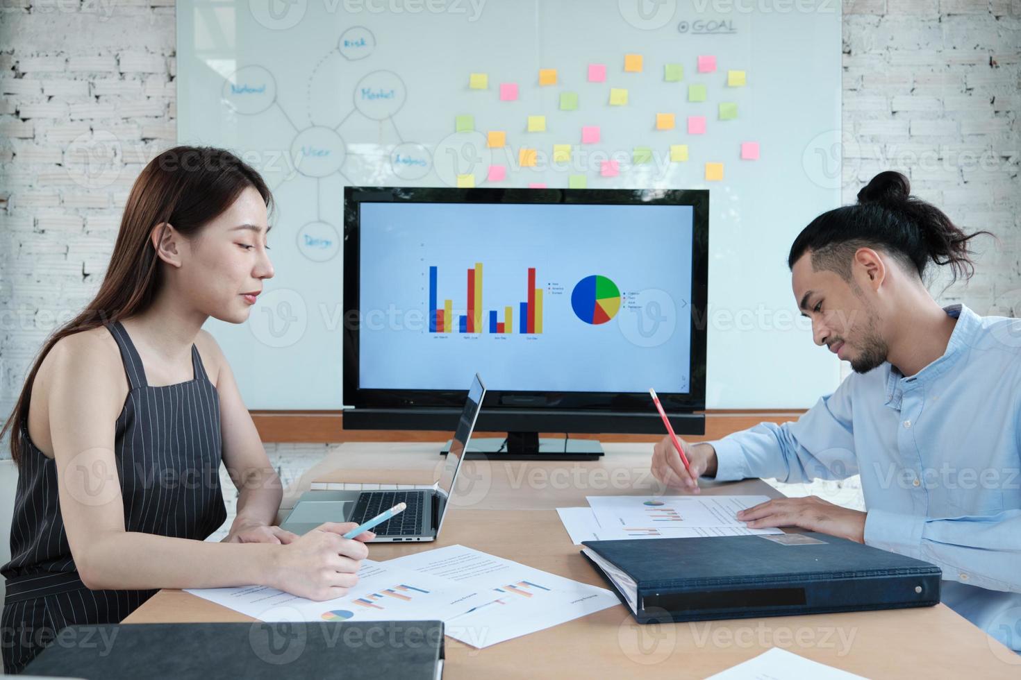 deux collègues et collègues d'ethnie asiatique réfléchissent à un projet de financement de la réunion et discutent avec des graphiques commerciaux dans une salle de conférence avec du papier collant coloré collé à bord dans le bureau. photo