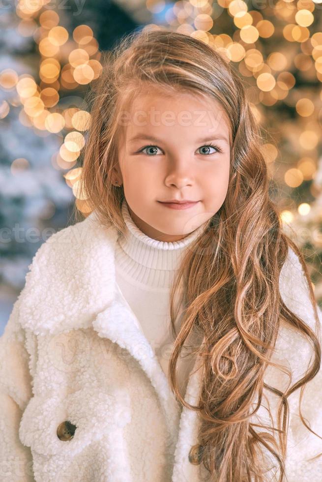 jolie fille blonde caucasienne en manteau de fourrure écologique blanc marchant dans la forêt de noël d'hiver avec des lumières. nouvel an, concept de conte de fées photo