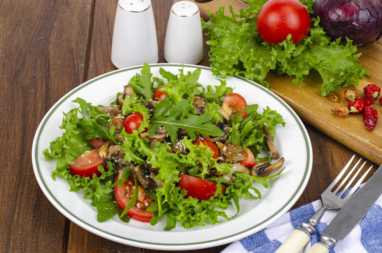 salade diététique de feuilles de roquette, tomates et champignons frits sur table en bois. studio photo