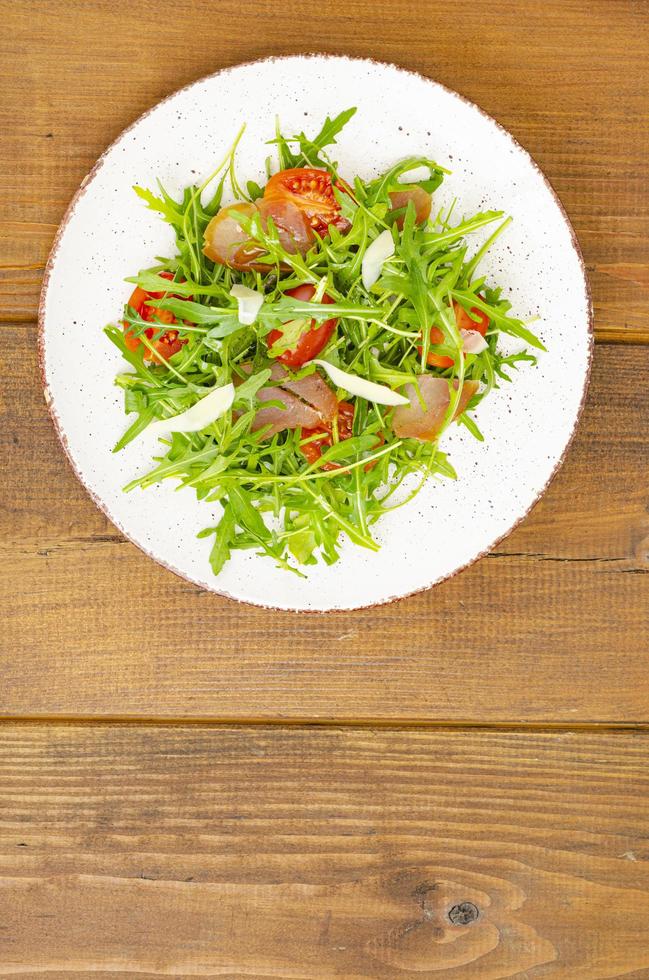 plat de roquette, tomates, viande séchée et fromage. salade sur plaque sur fond de bois photo