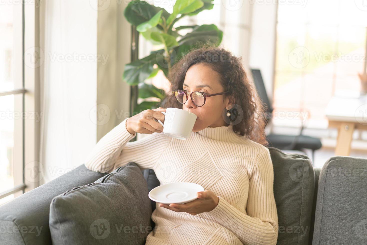 femme latine buvant du café sur un canapé à la maison photo