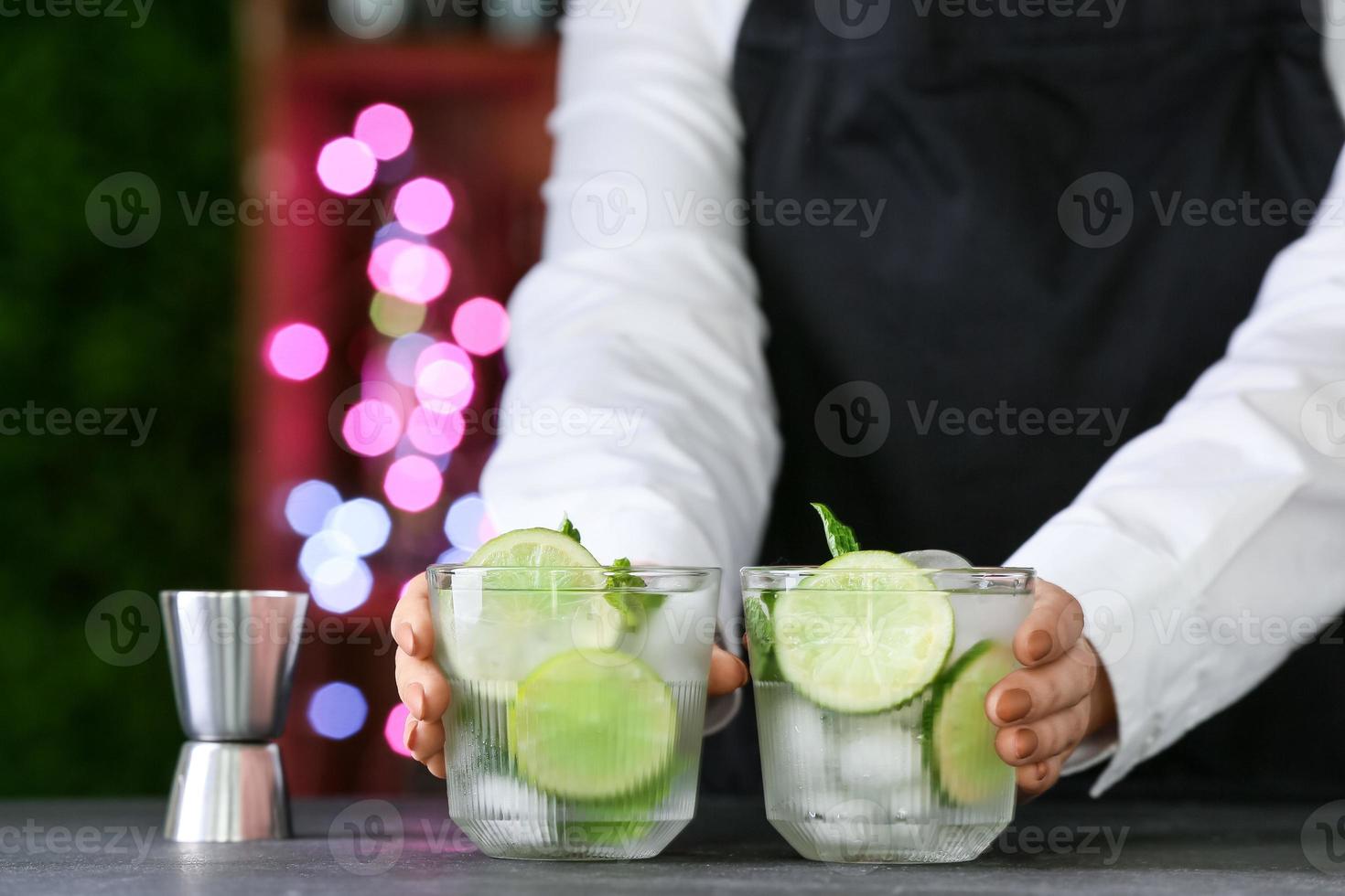 barman féminin avec des verres de mojito frais sur table en bar photo