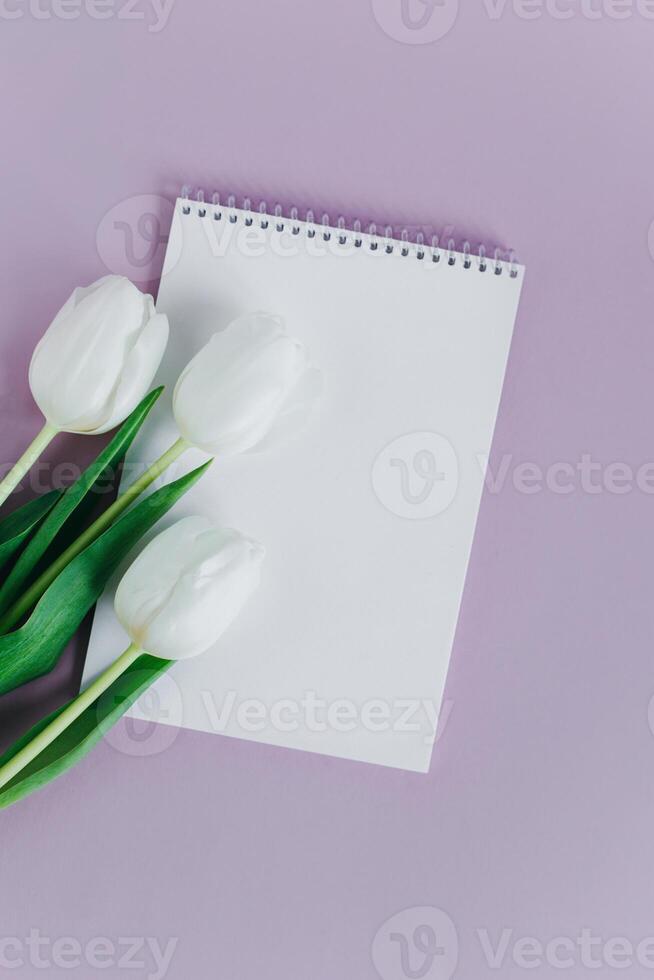 magnifique blanc tulipes et carnet avec Vide page sur violet pastel Contexte. photo