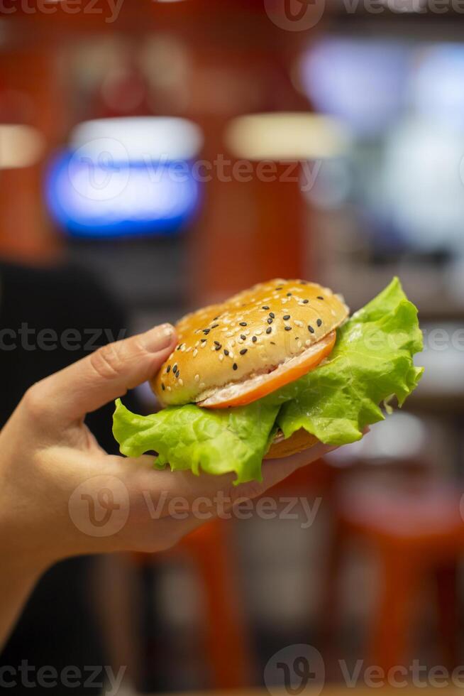 mains en portant une Hamburger saupoudré avec sésame des graines sur une flou Contexte. photo