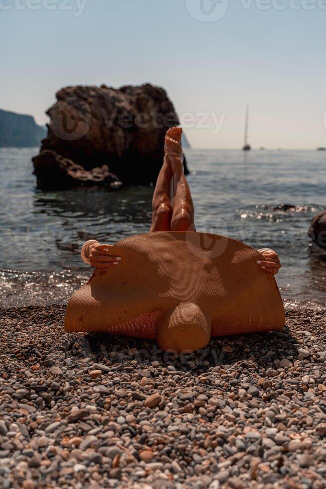 une magnifique âge moyen femme mensonges sur le plage avec sa pieds à le ciel, couvrant sa corps avec une à larges bords paille chapeau. elle est bain de soleil sur le océan. vacances, voyage, vacances concept. photo