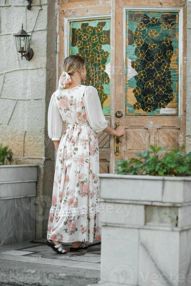 une femme dans une fleur robe ouvre le porte à le maison photo