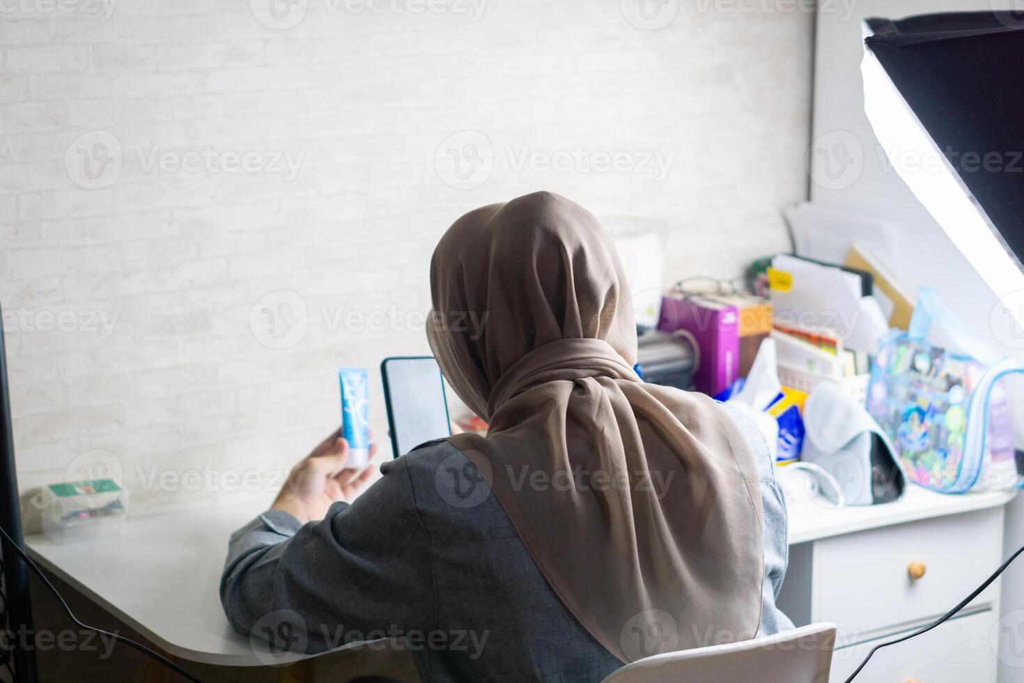 femme avec hijab est travail avec mobile téléphone à faire une et produire contenu pour vente produit photo