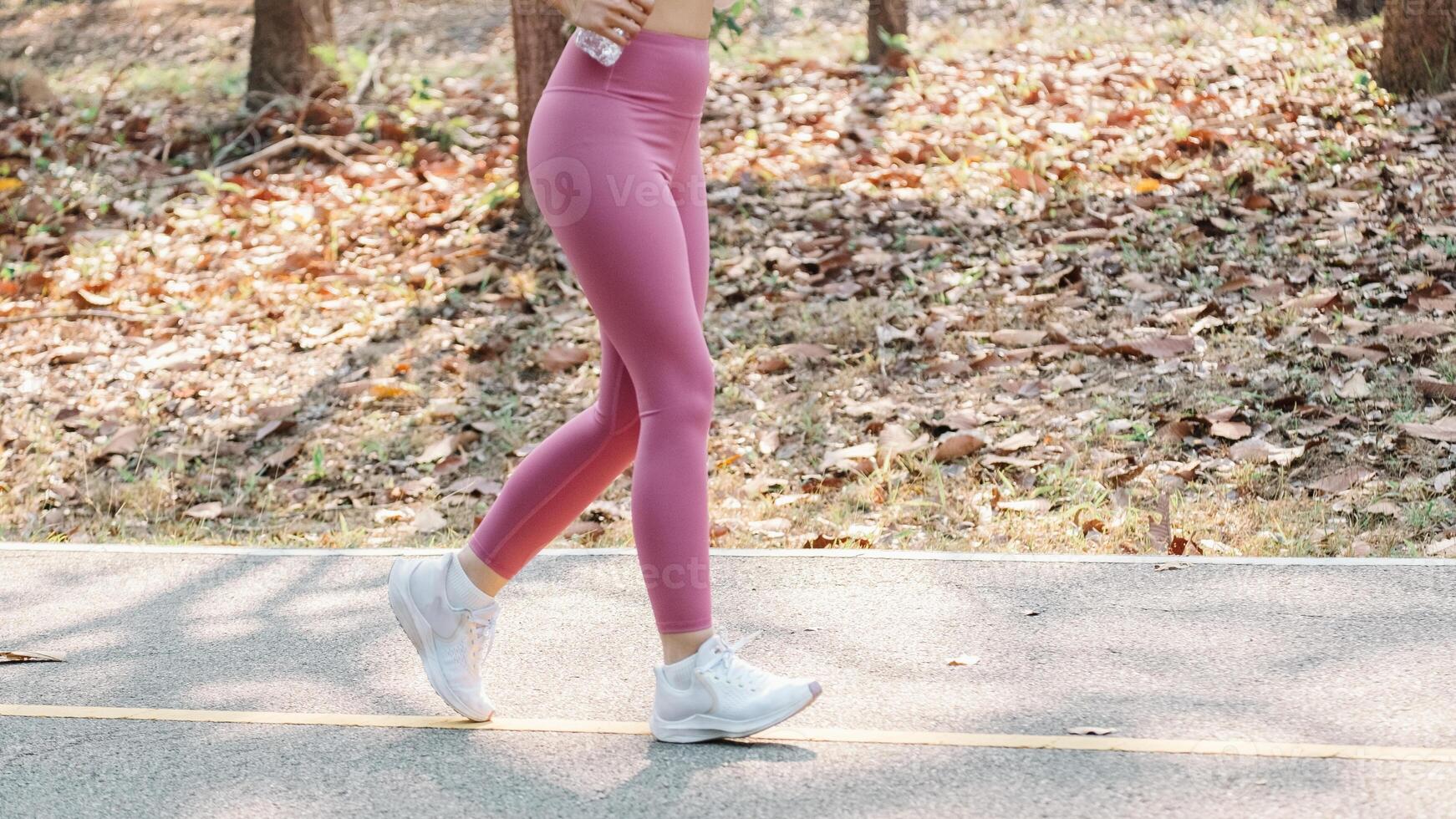 femme jambes dans rose leggings, le jogging sur une parc sentier entouré par déchue feuilles. photo