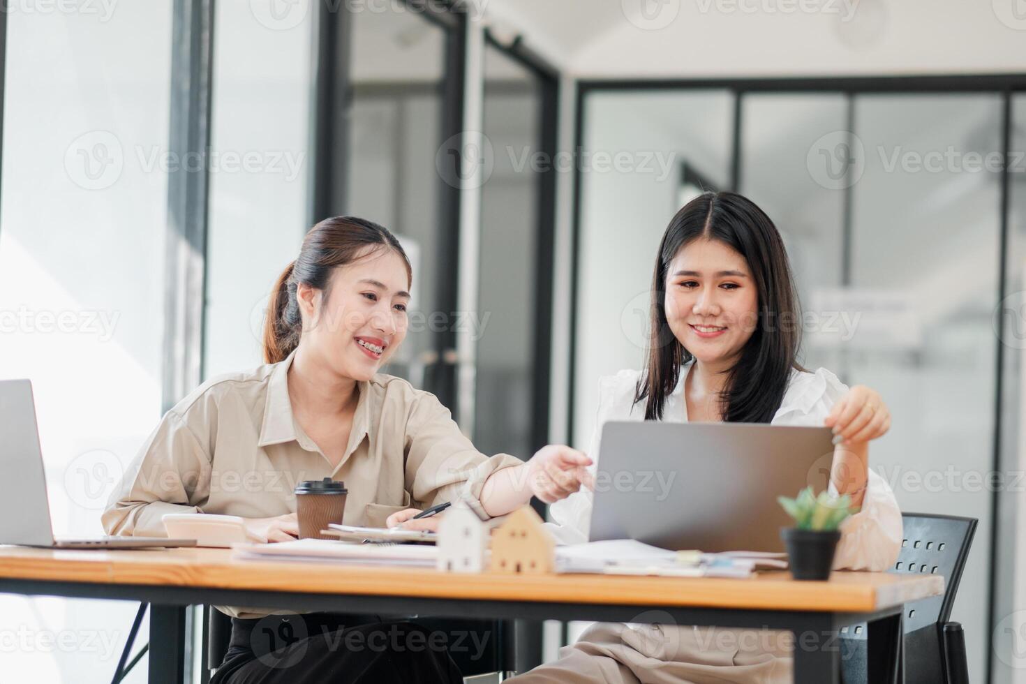 deux femmes engager dans une amical discussion plus de une ordinateur portable, avec un montrer du doigt à le filtrer, à un Bureau table avec café et papeterie. photo