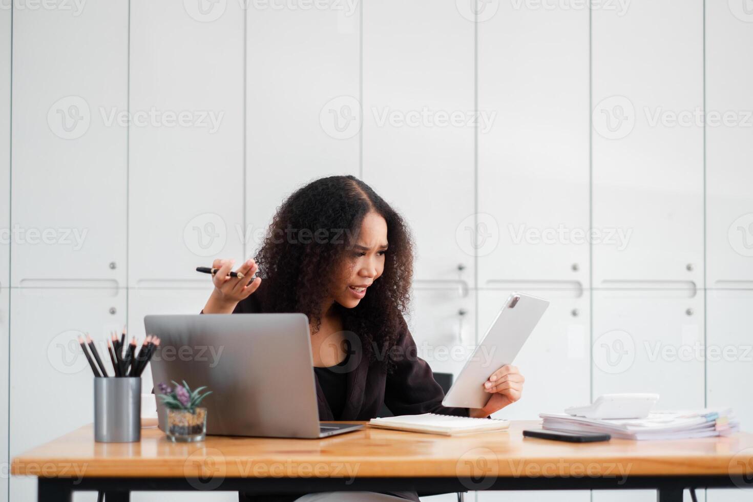joyeux femme d'affaires est surpris comme elle lit positif nouvelles sur sa tablette à sa espace de travail, avec une portable et Stationnaire sur sa bureau. photo