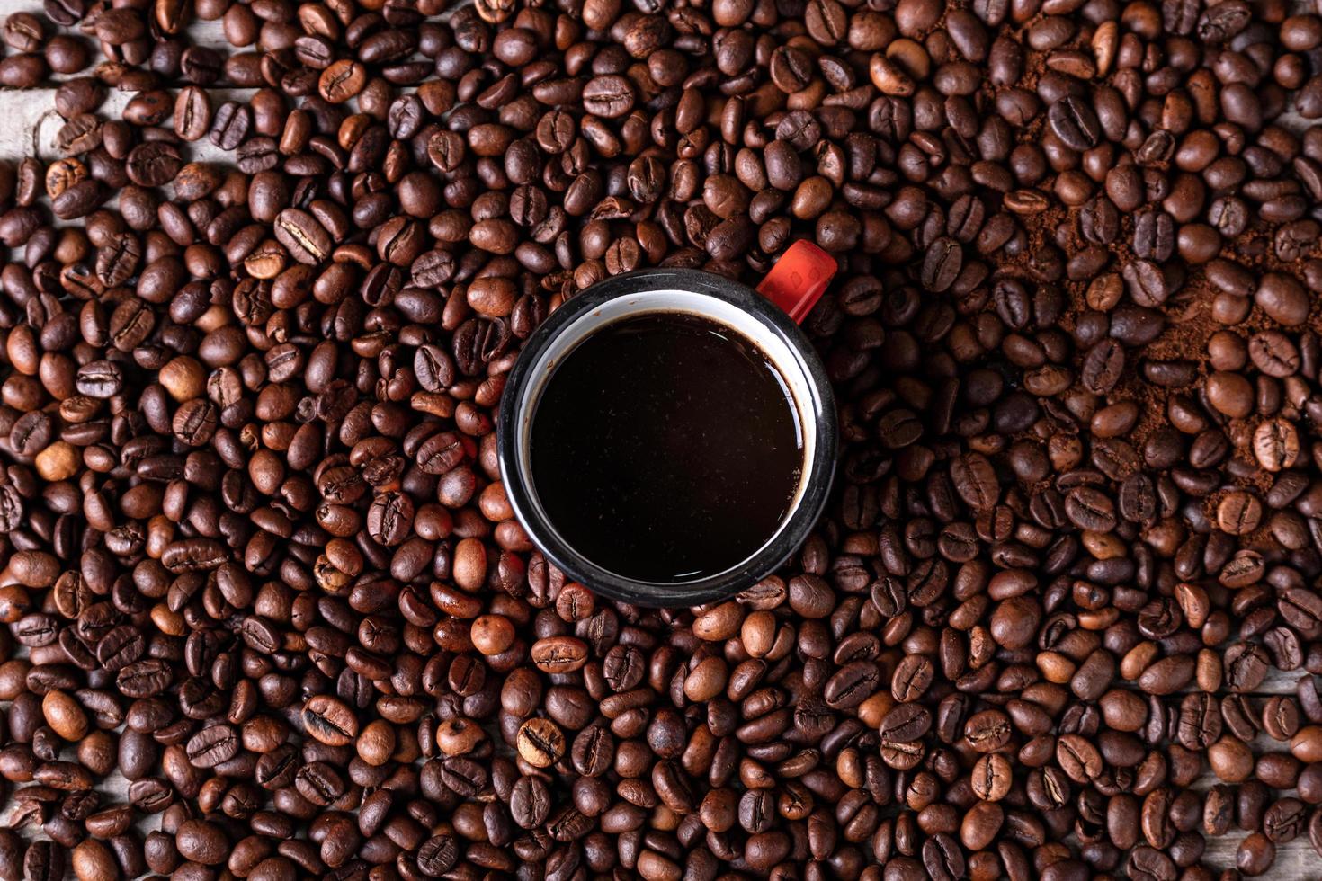 fond de grains de café avec une tasse en métal rouge au centre avec du café fraîchement préparé photo