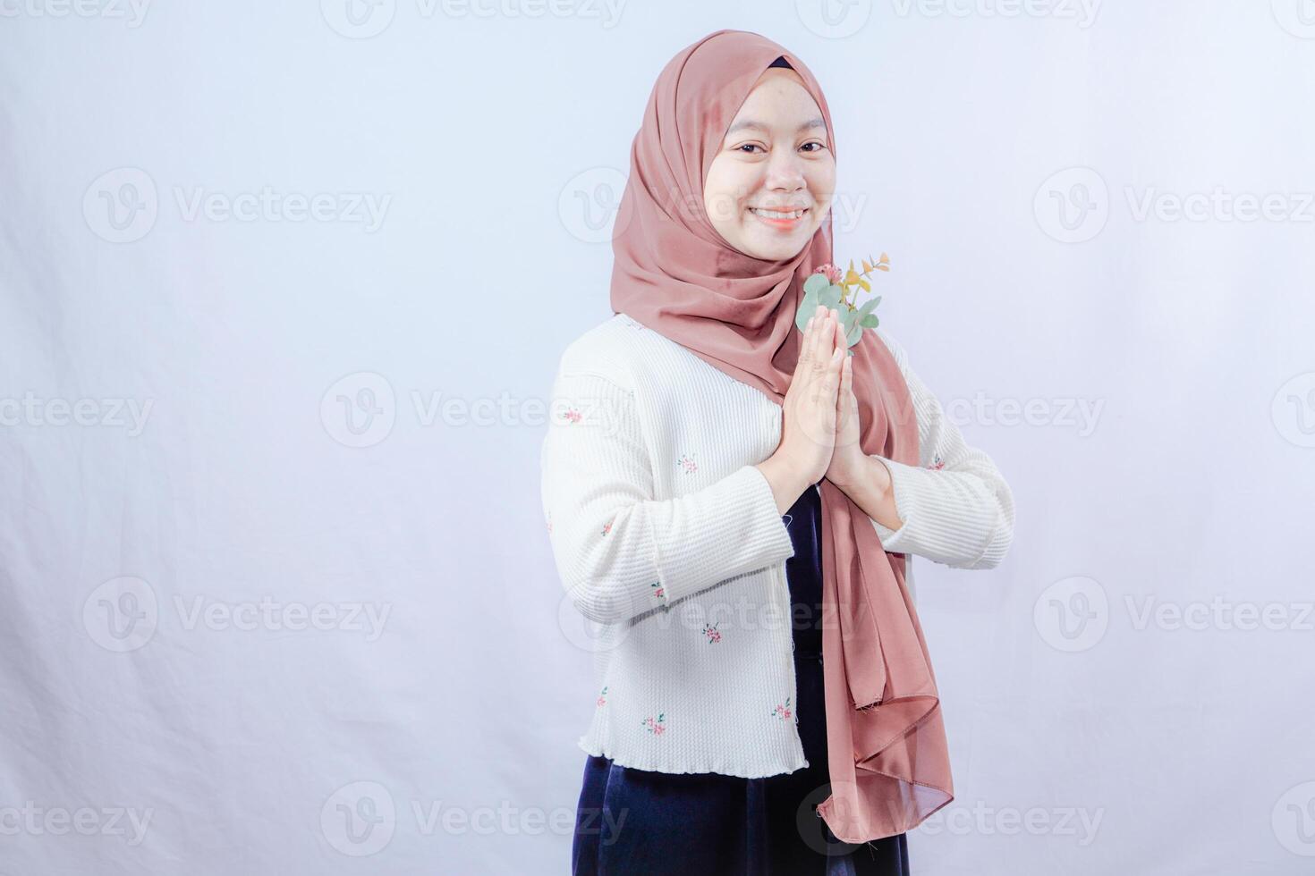 une femme portant une foulard est donnant une salutation par en portant fleurs dans de face de sa poitrine, sur une blanc Contexte avec vide espace pour publicité. photo