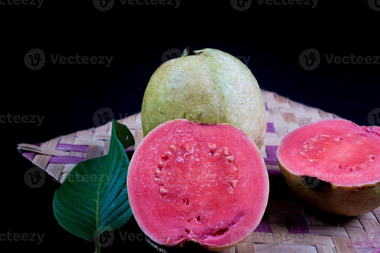 goyave isolé. collection de rouge charnu goyave fruit avec jaunâtre vert peau et feuilles isolé sur noir Contexte avec tissé bambou. photo