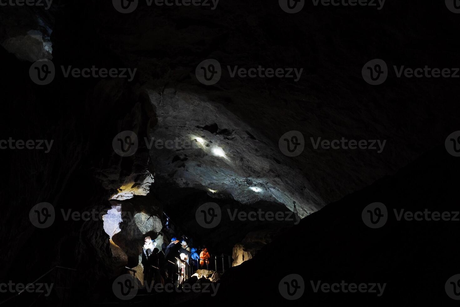 souterrain karst la grotte une groupe de gens inspecter le coffres de le ancien habitation de une Homme des cavernes, touristes Aller sur excursions souterrain, le lumière de le lampe frontale. photo