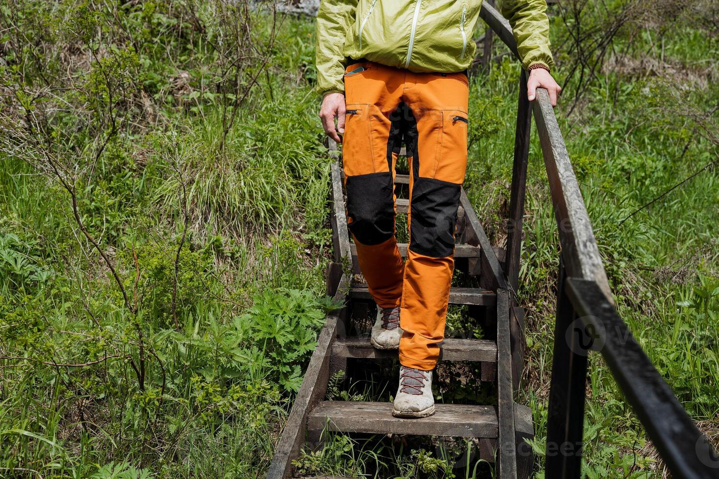 jambes dans Orange un pantalon aller vers le bas le pas. une homme des promenades dans touristique des chaussures sur en bois pas, le balustrade tenue par main. photo