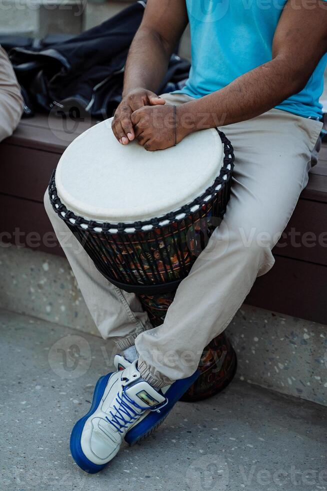 un Afro-américain pièces une tambouriner, le mains de une noir gars mensonge sur le blanc plate-forme de un africain djembé tambouriner, une rue musicien, une partie de une Humain corps. photo