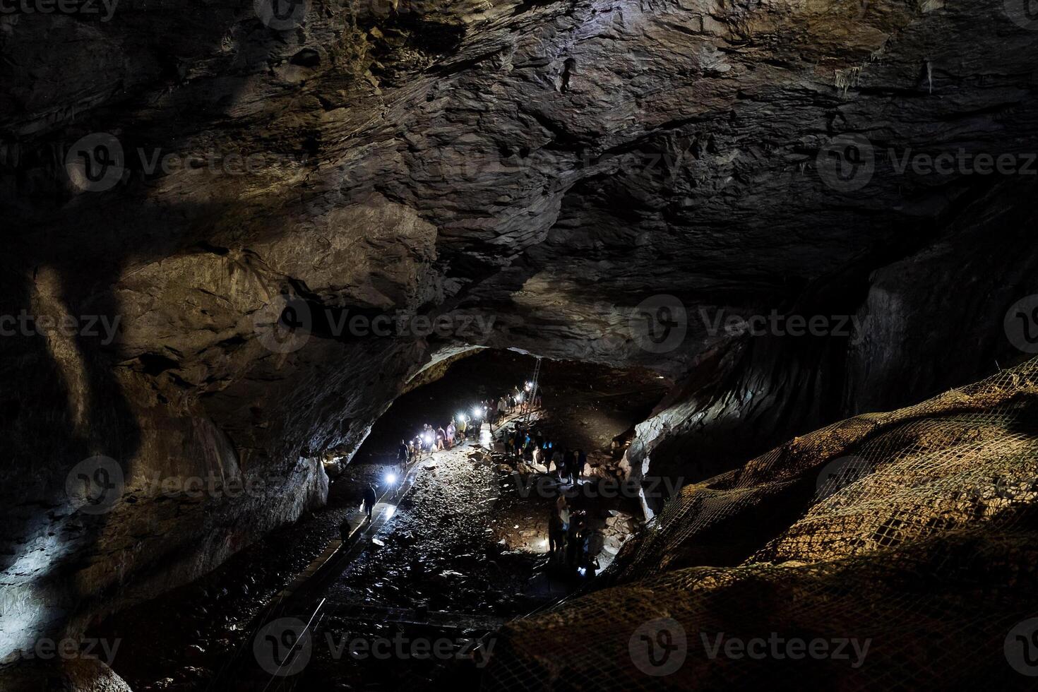 le pierre coffres de le grotte, le lumière illumine le plafond de le karst grotte, une groupe de gens aller à inspecter le gypse grotte, une géant souterrain passage. photo